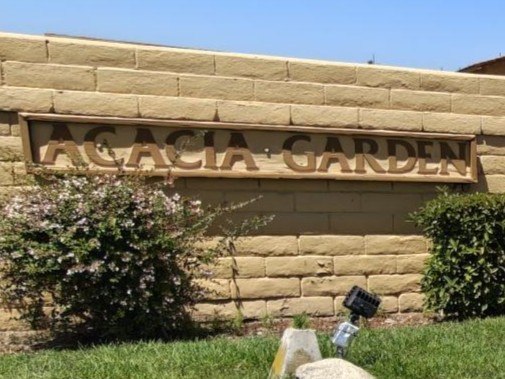 A sign that says "Acacia Garden" is mounted on a tan wall.